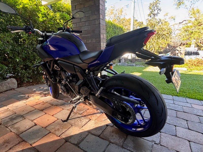 Blue and black motorcycle parked on a brick driveway with greenery in the background