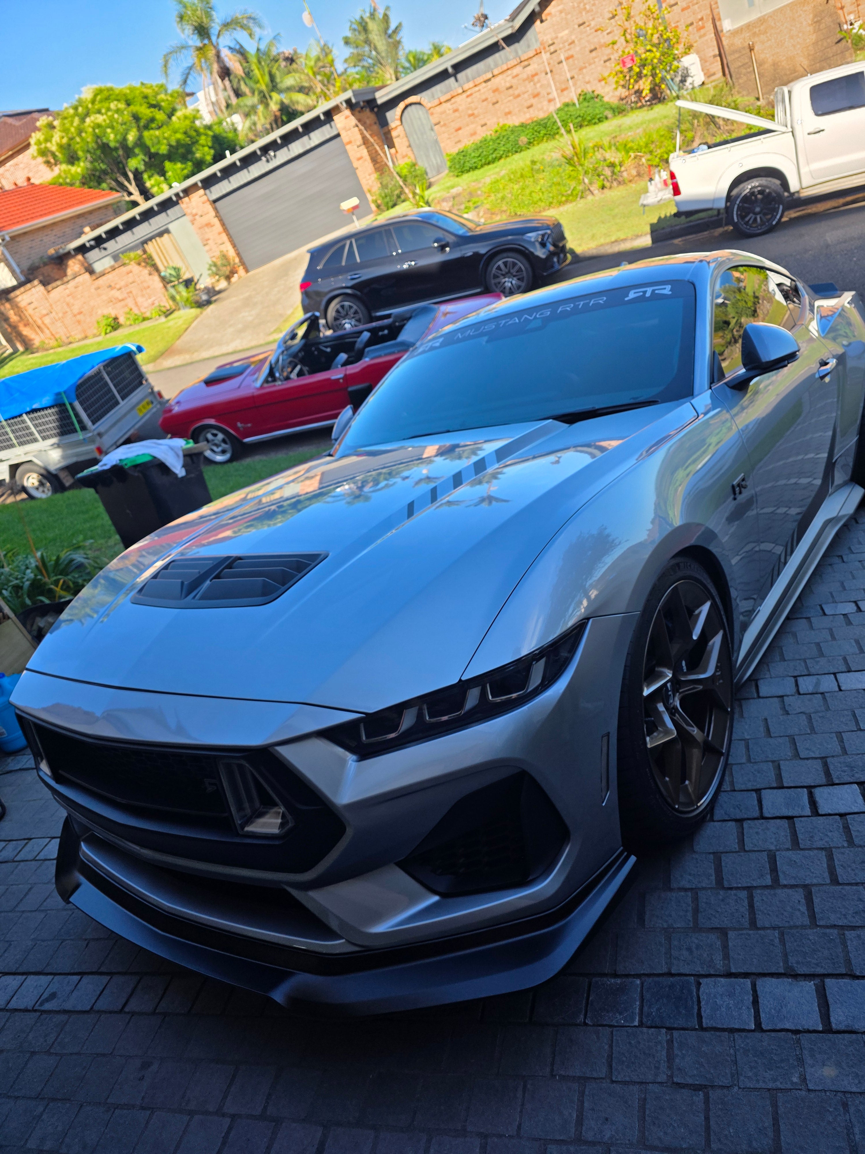 Gray sports car parked on a driveway with other cars in the background