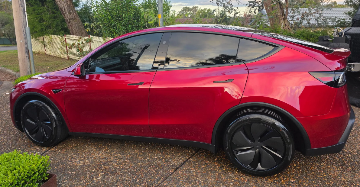 Red Tesla Model Y parked on a driveway with a garden and house in the background