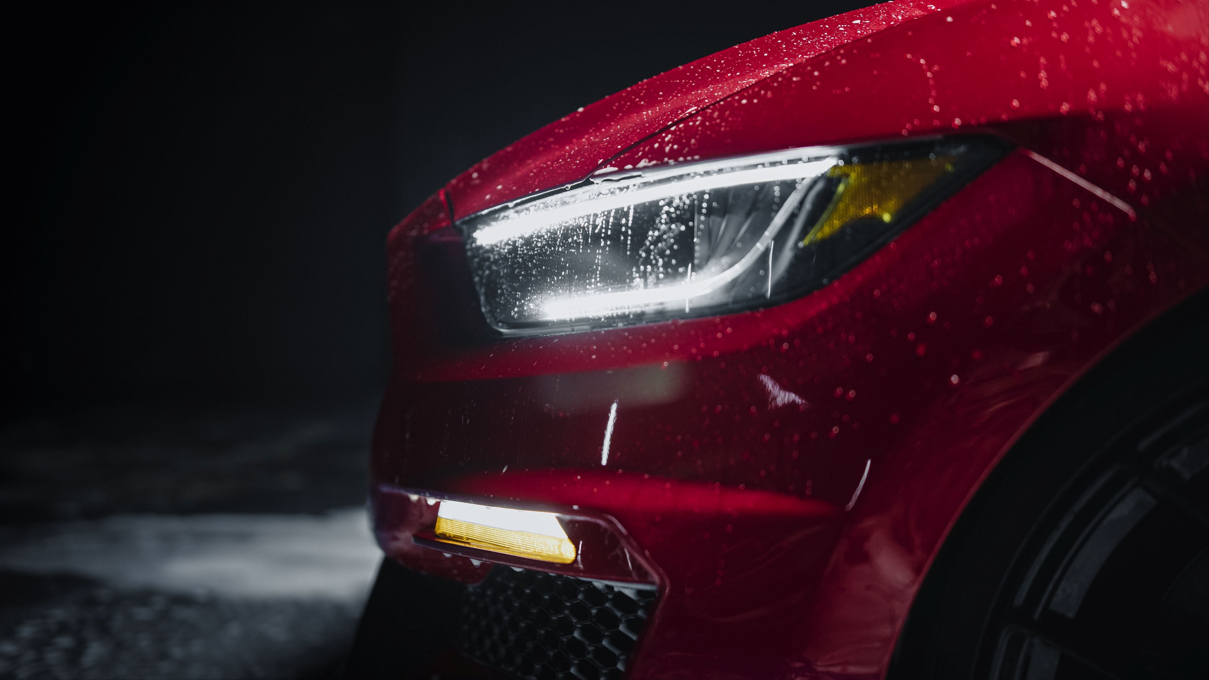 Close-up of a red car's headlight with water droplets on a dark background