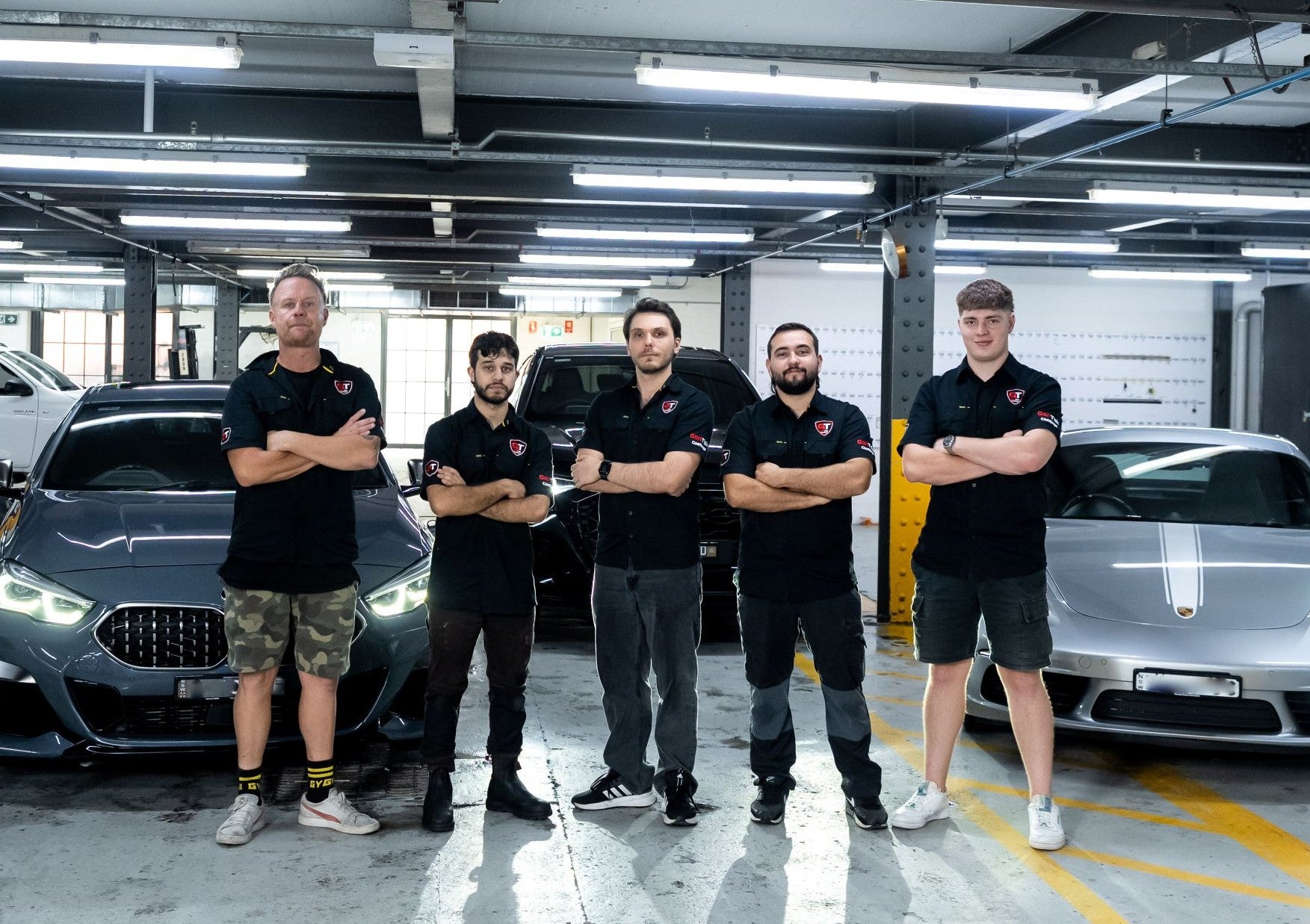 Five GenTek car protection specialists in uniform standing together with luxury vehicles in the background.
