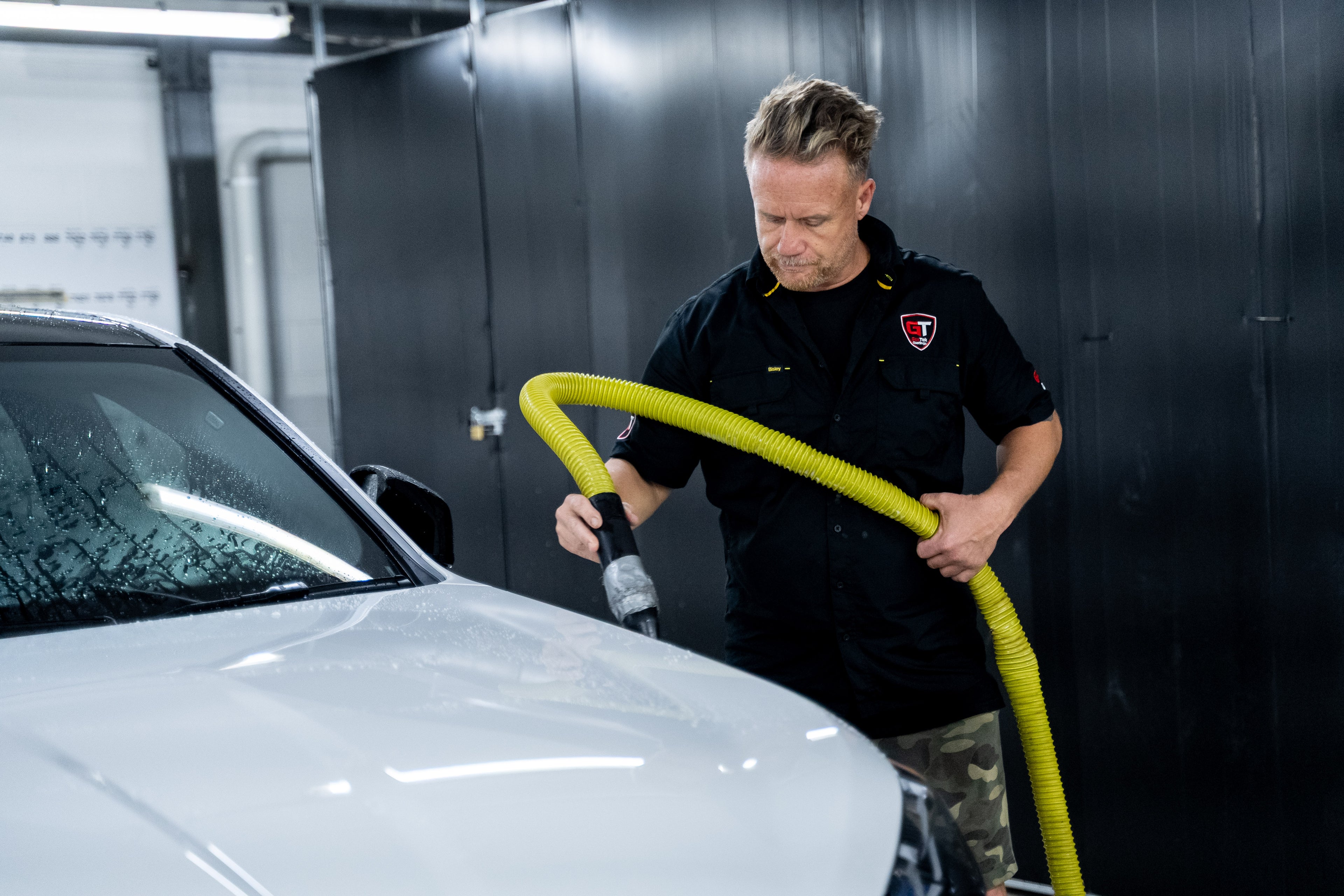 GenTek technician using filtered air to dry a silver car during professional paint preparation.