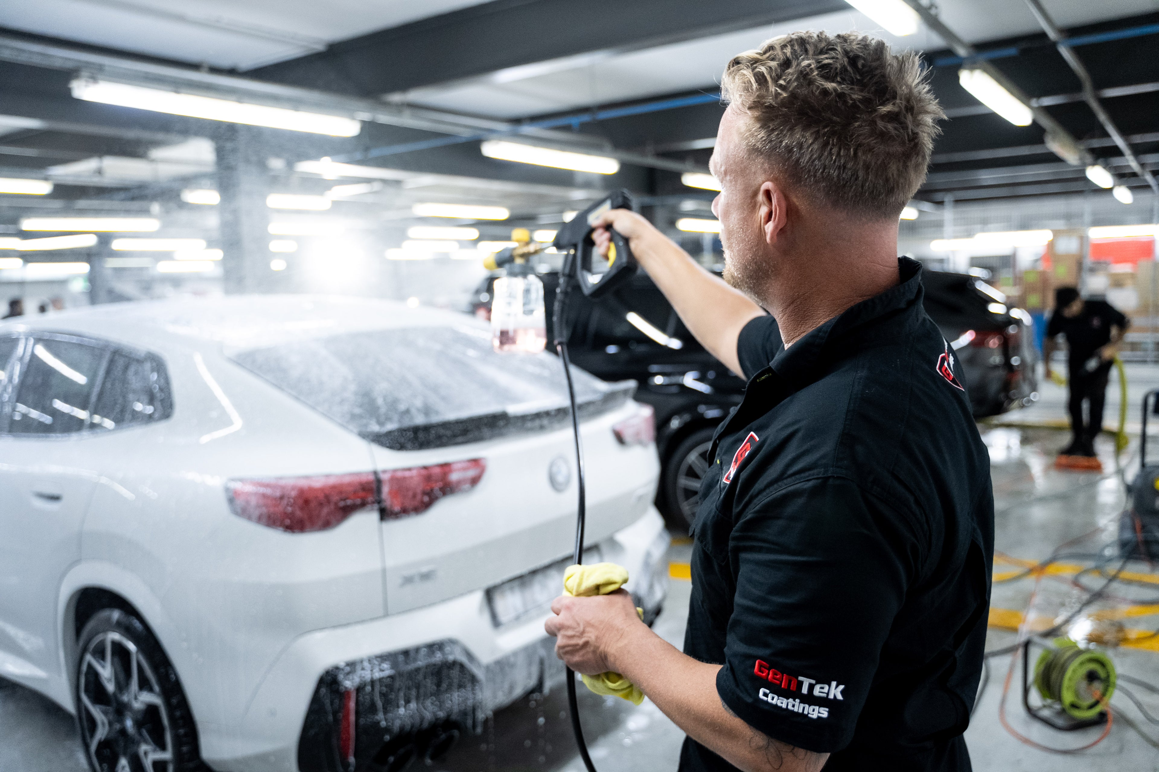 GenTek technician applying cleaning solution to a white SUV during professional vehicle preparation.