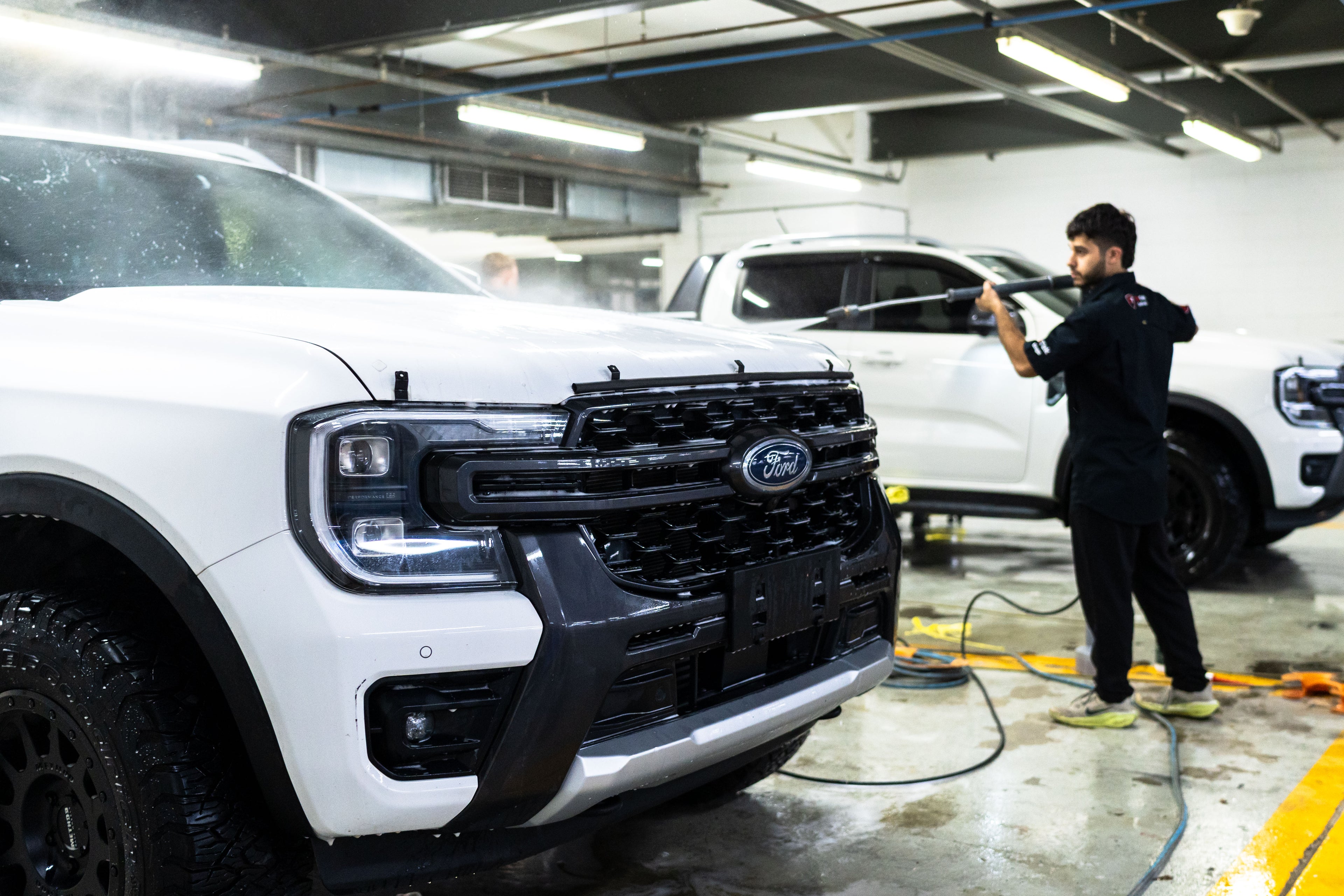 GenTek technician pressure washing a white Ford ute during professional vehicle preparation.