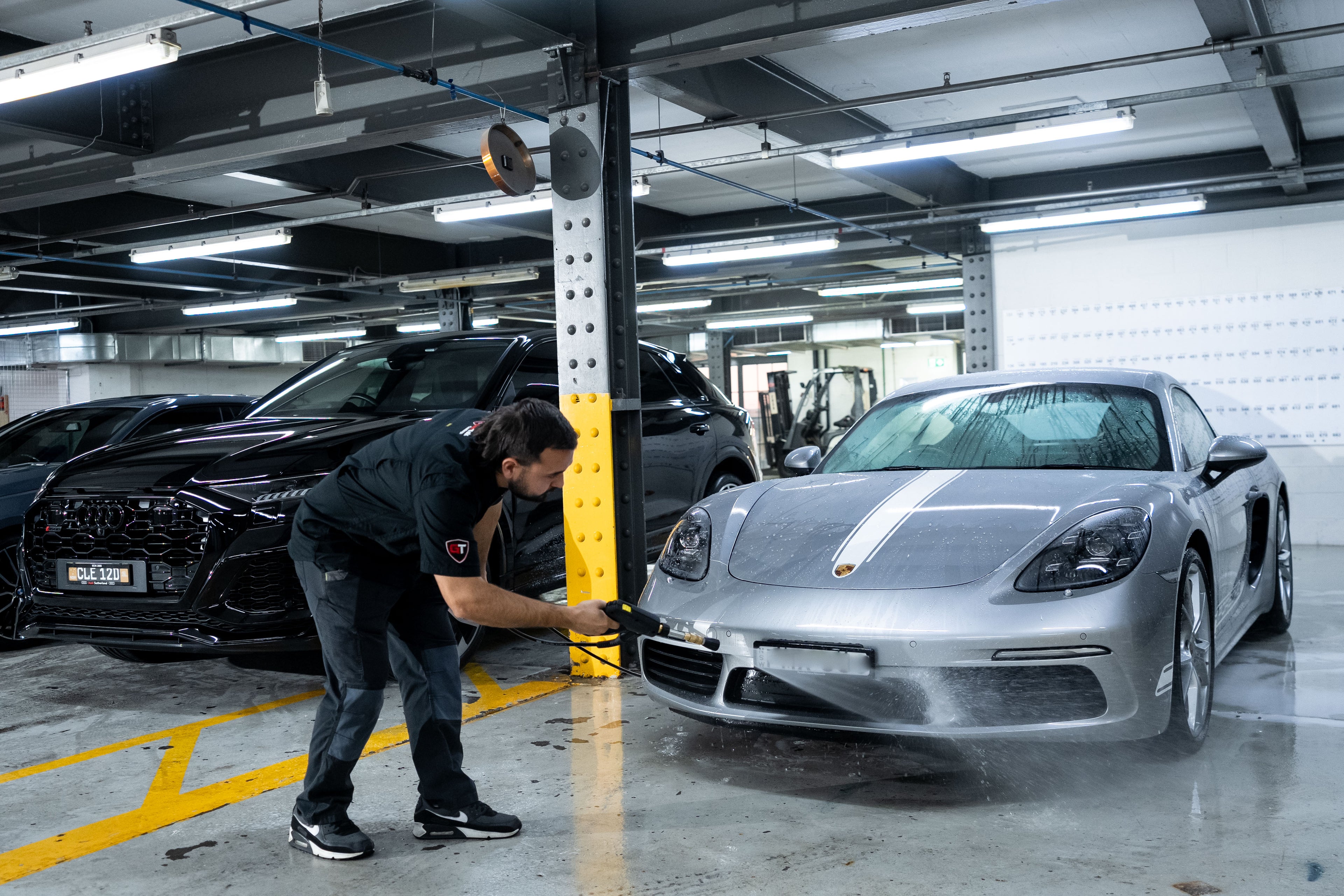 GenTek technician pressure washing a silver Porsche during professional vehicle preparation.