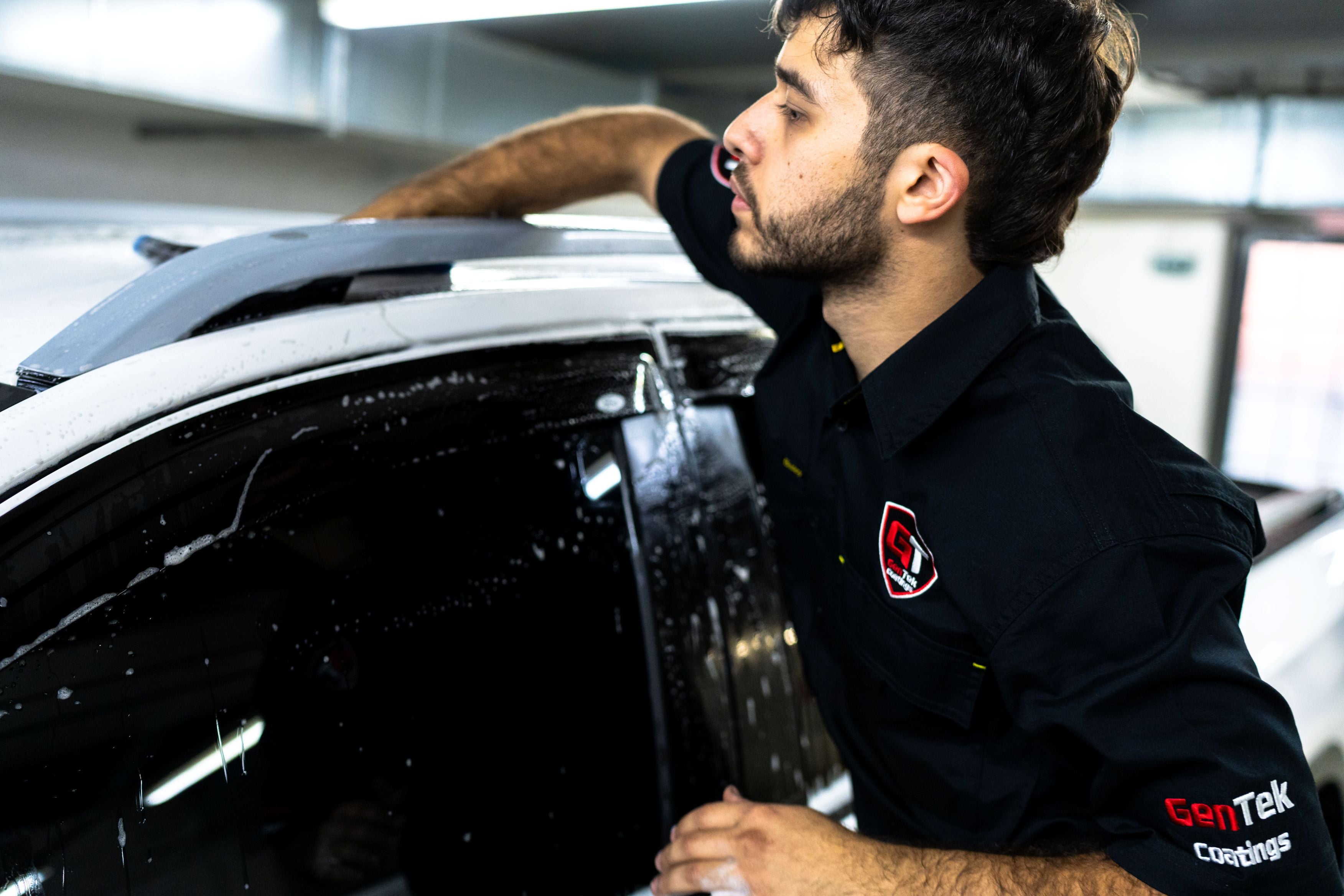 GenTek technician hand washing the roof of a white ute during professional vehicle preparation.